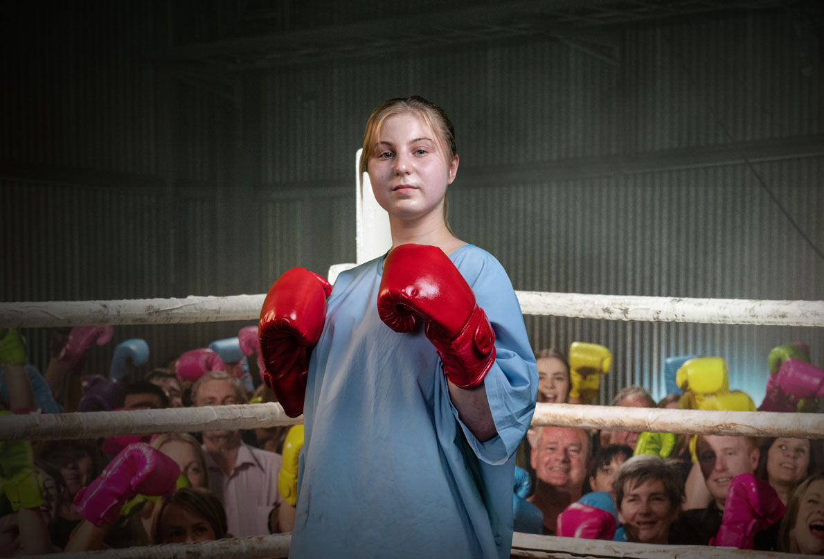 Image of young female hospital patient standing with bright red boxing gloves in boxing ring