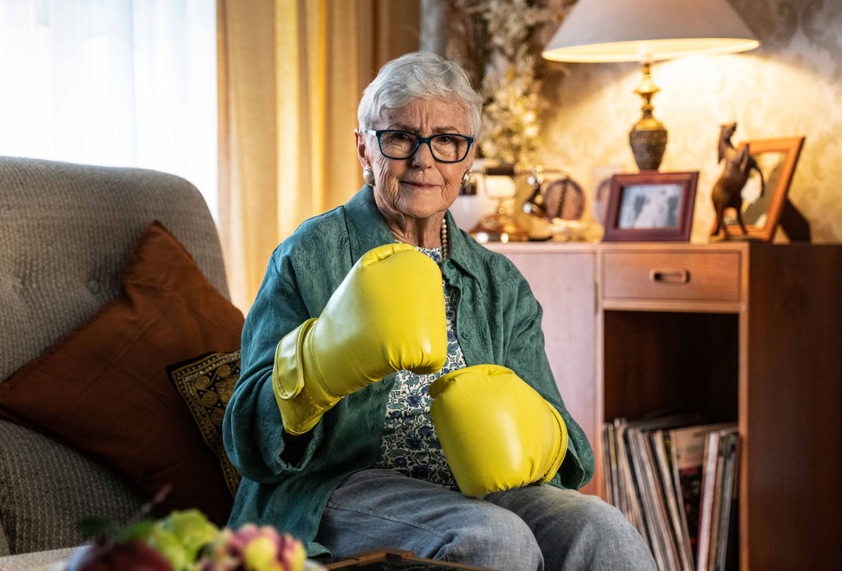 Image of older female sitting at home with bright yellow boxing gloves