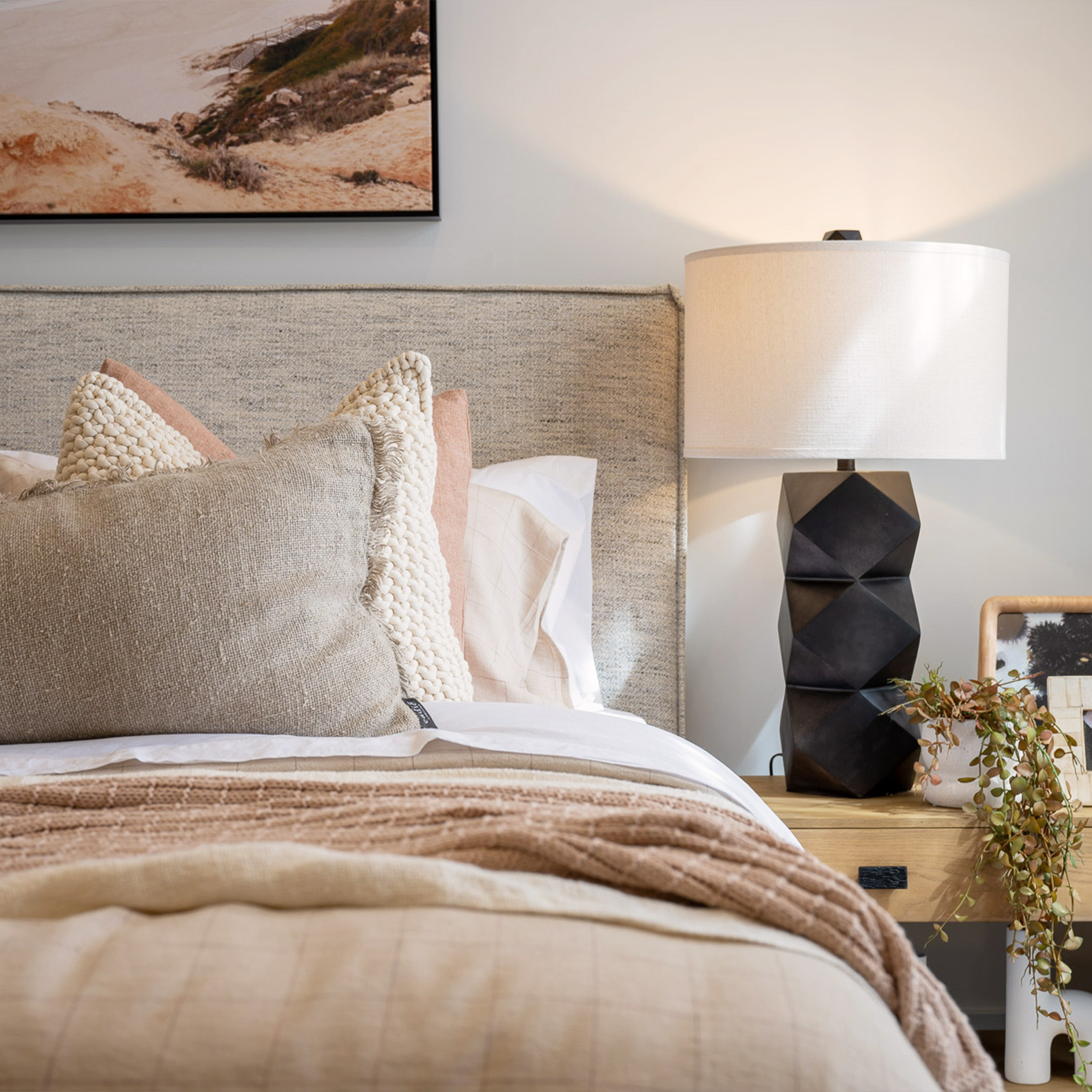 Close up of bed with soft beige and coral coloured linen and black side table lamp