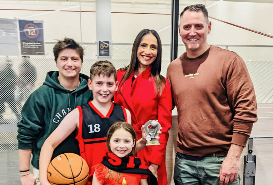 Family of five smiling together, one of the children holds a basketball and a trophy