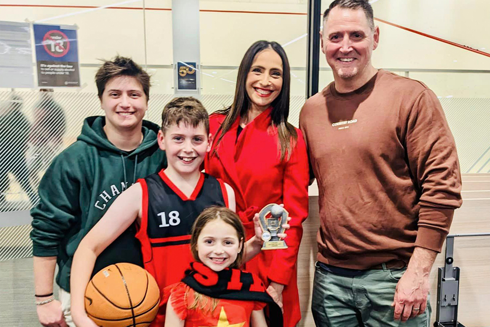 Family of five smiling together, one of the children holds a basketball and a trophy