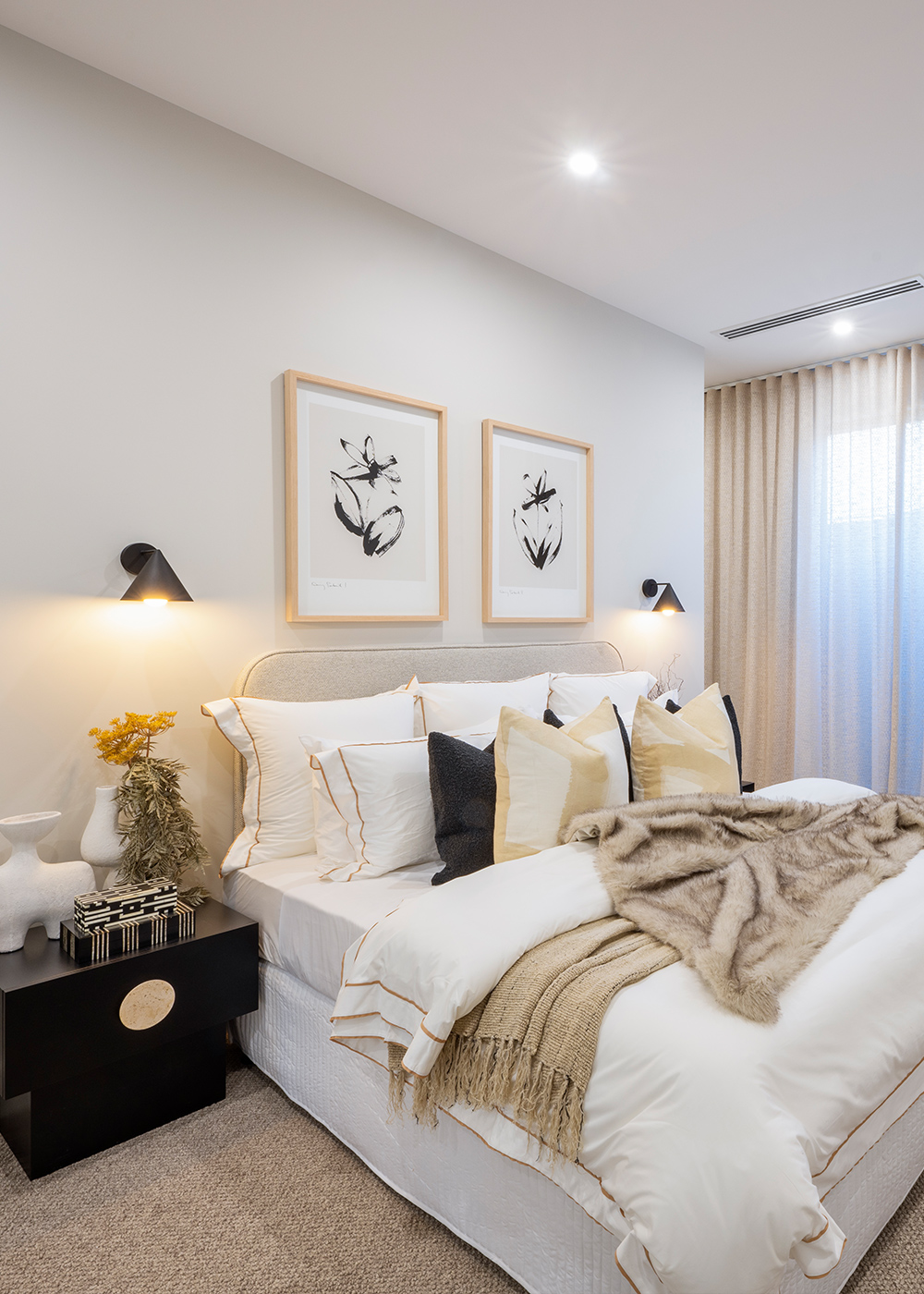 Master bedroom with large central bed with layers of throw rugs and decorative cushions in shades of cream.