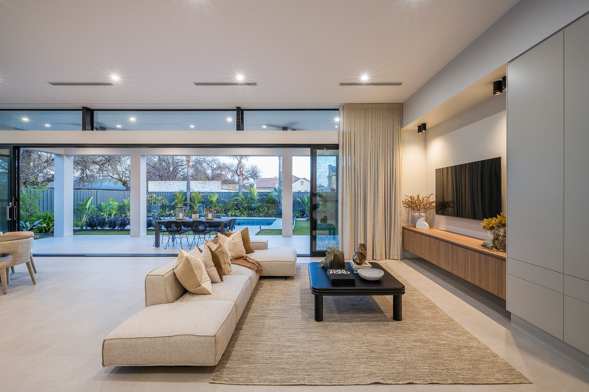 Open plan living area with couch, coffee table and wall mounted tv, beyond the sliding doors are open to the backyard