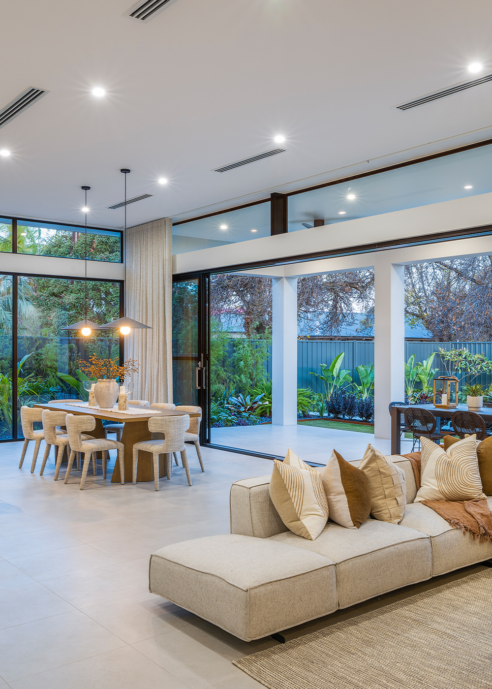 Living and dining area of the open plan living zone, full height windows look out to a lush side garden