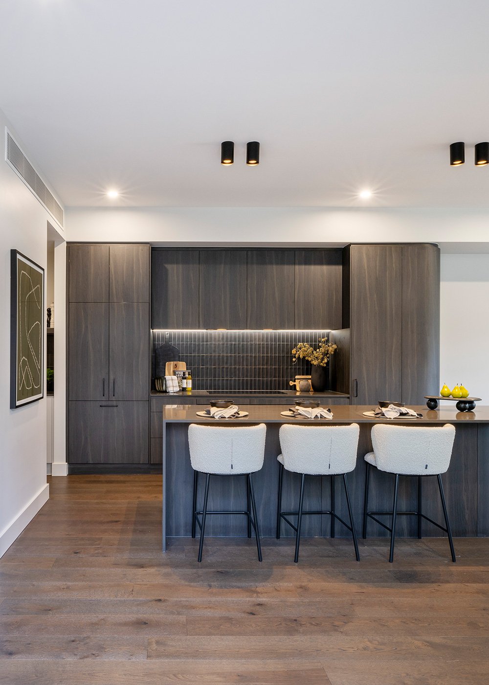 Kitchen with dark timber cabinetry and 3 white bench seats with place settings